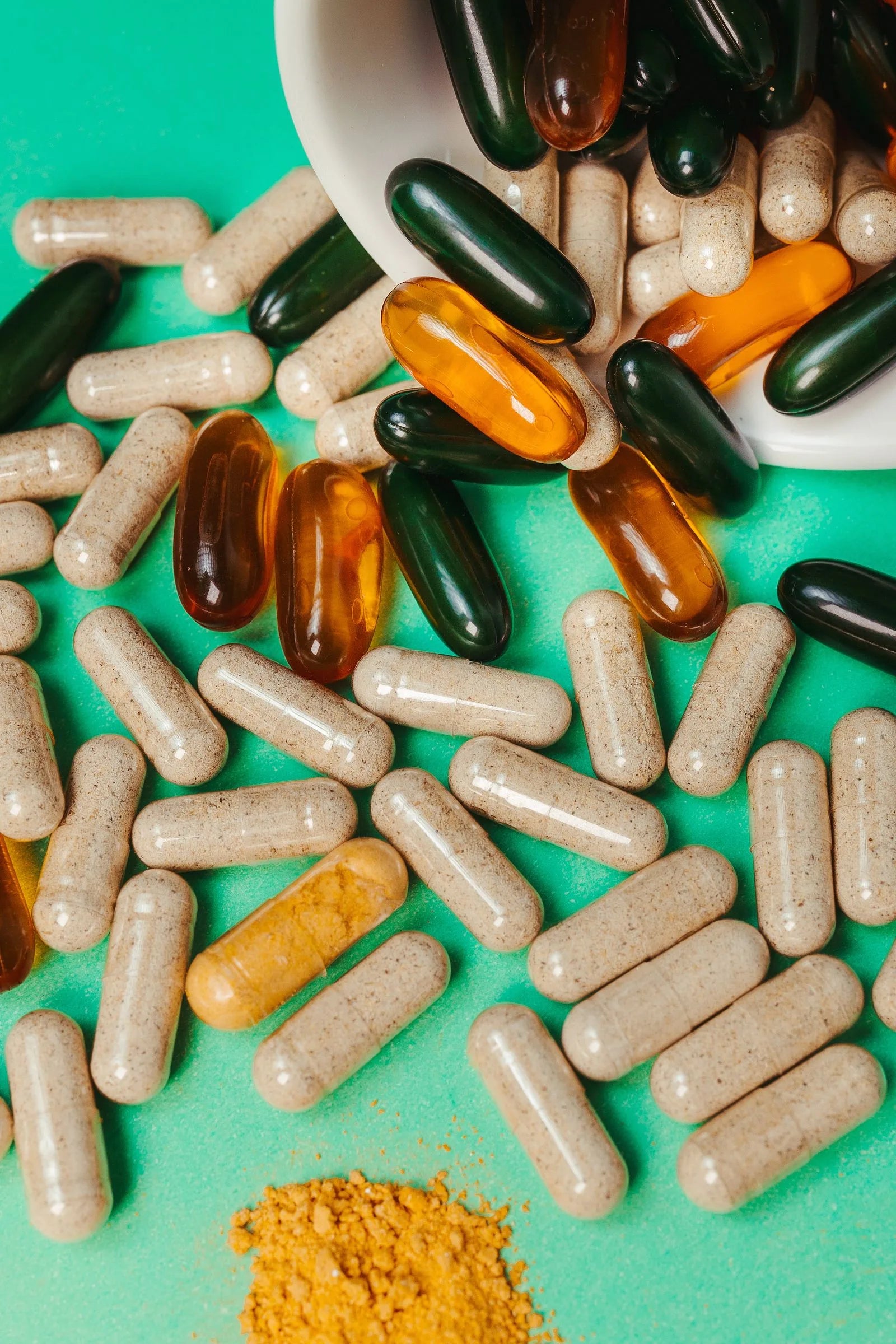 Close-up of assorted biotin and vitamin supplement capsules and softgels scattered on a green surface, representing hair growth supplementation