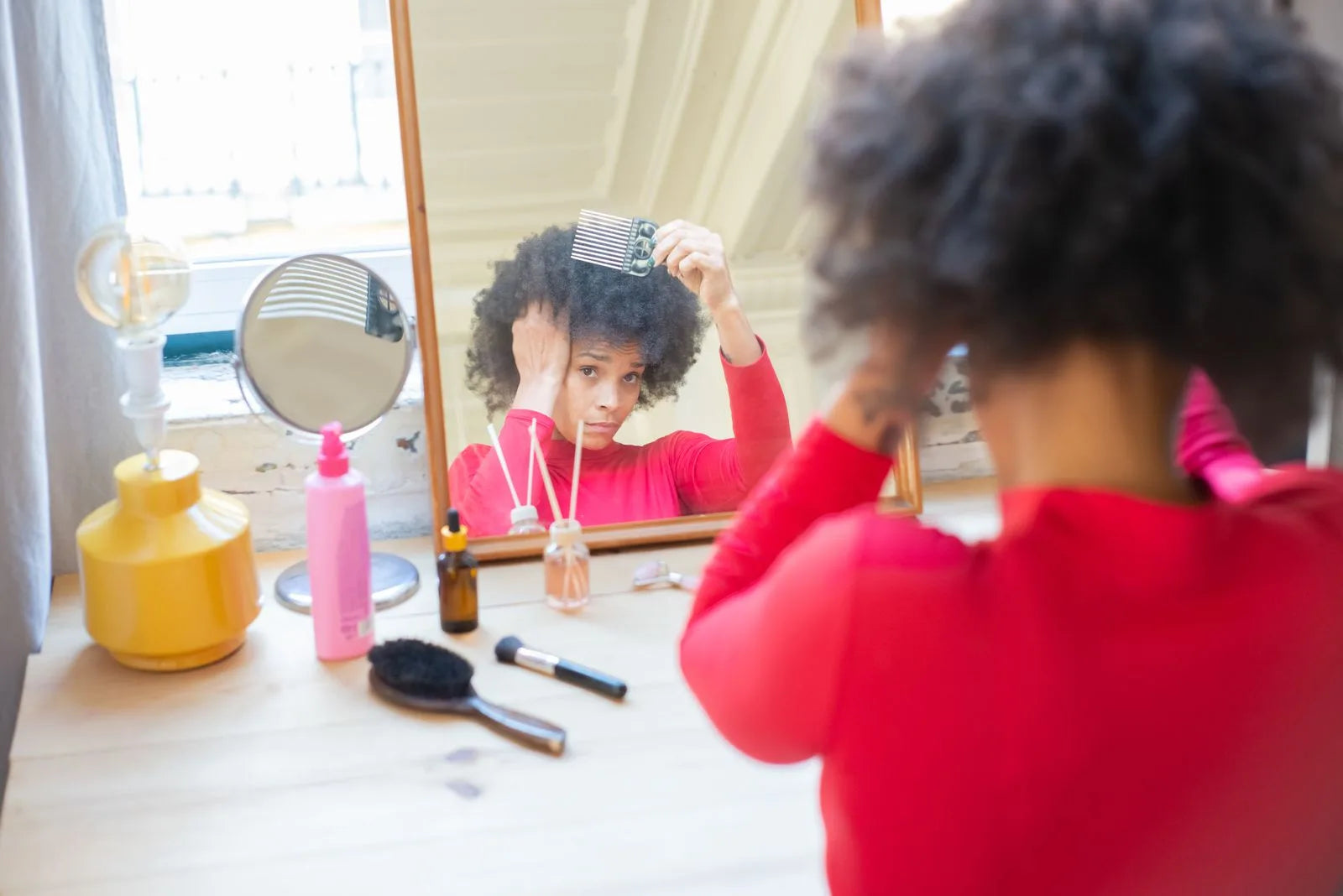 Woman combing and examining her hair in front of a mirror indoors