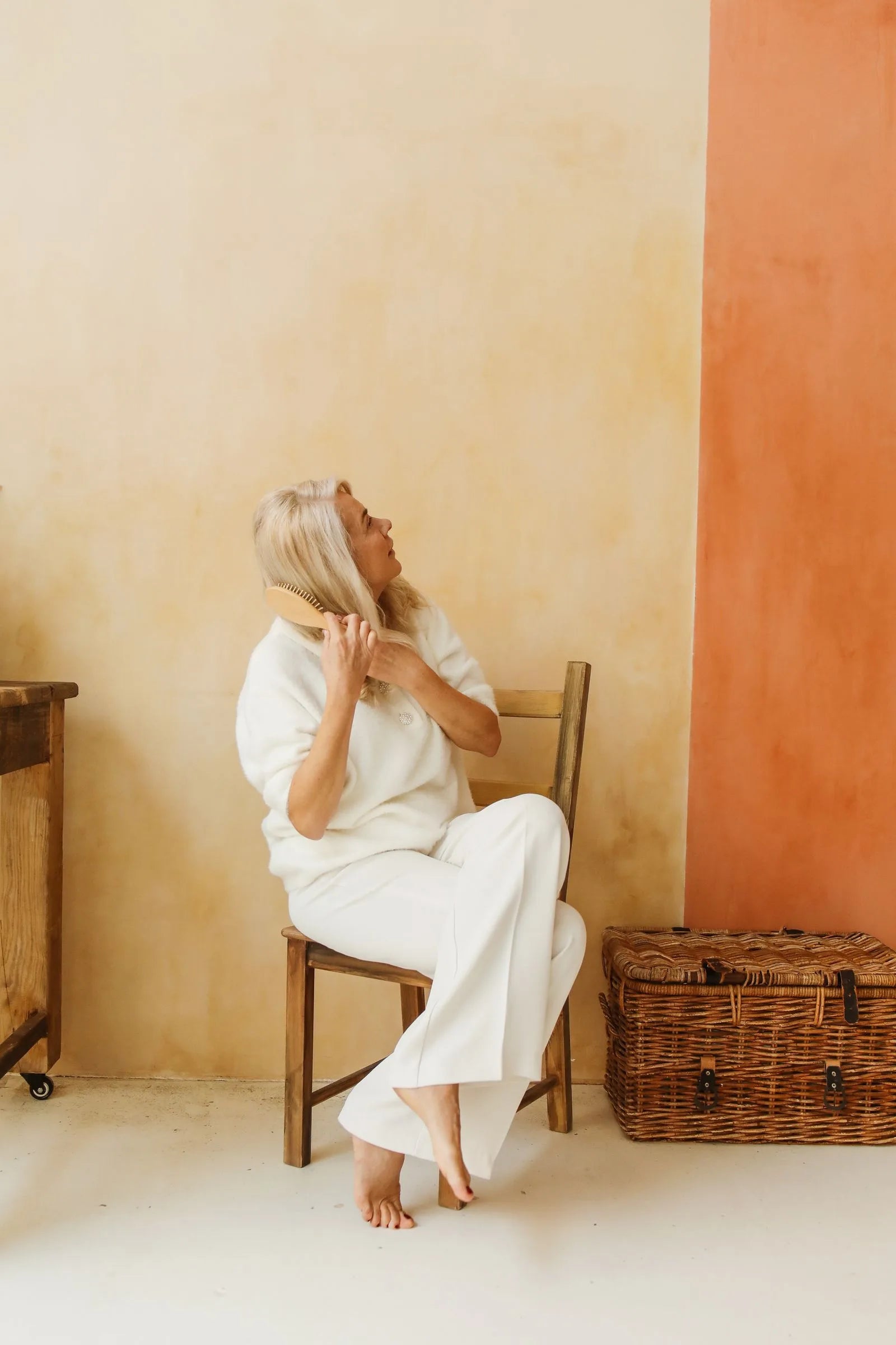 Senior woman sitting on a wooden chair brushing her long gray hair with a wooden hairbrush