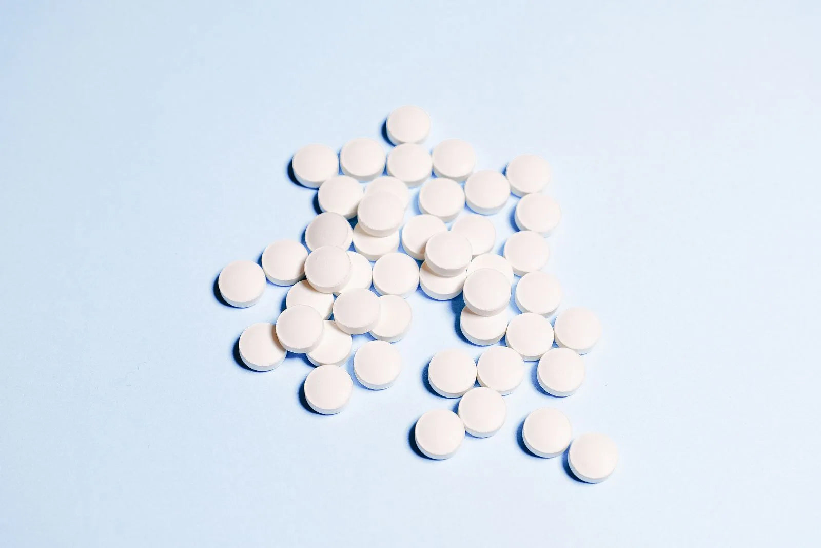 Close-up flat lay of white round medication pills scattered on a light blue surface, representing a finasteride prescription for hair loss treatment