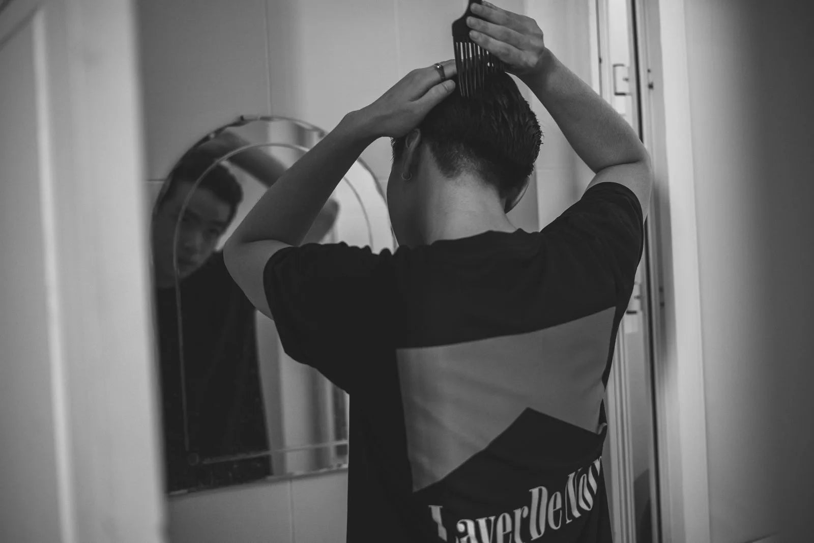 Man combing his hair in front of a bathroom mirror during his morning grooming routine