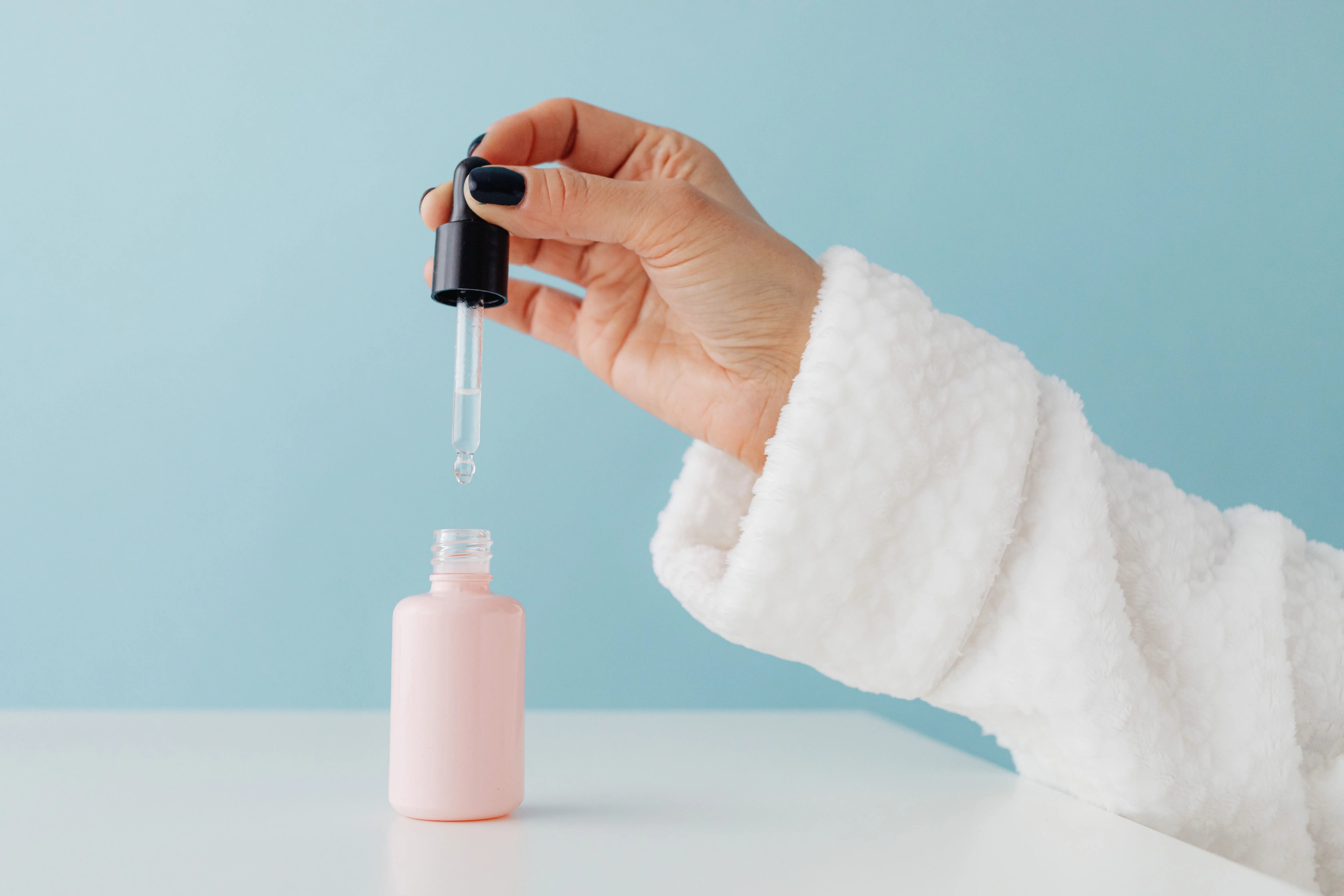 Close-up of a hand using a glass dropper to apply topical serum into an unbranded bottle, representing a topical DHT blocker application routine