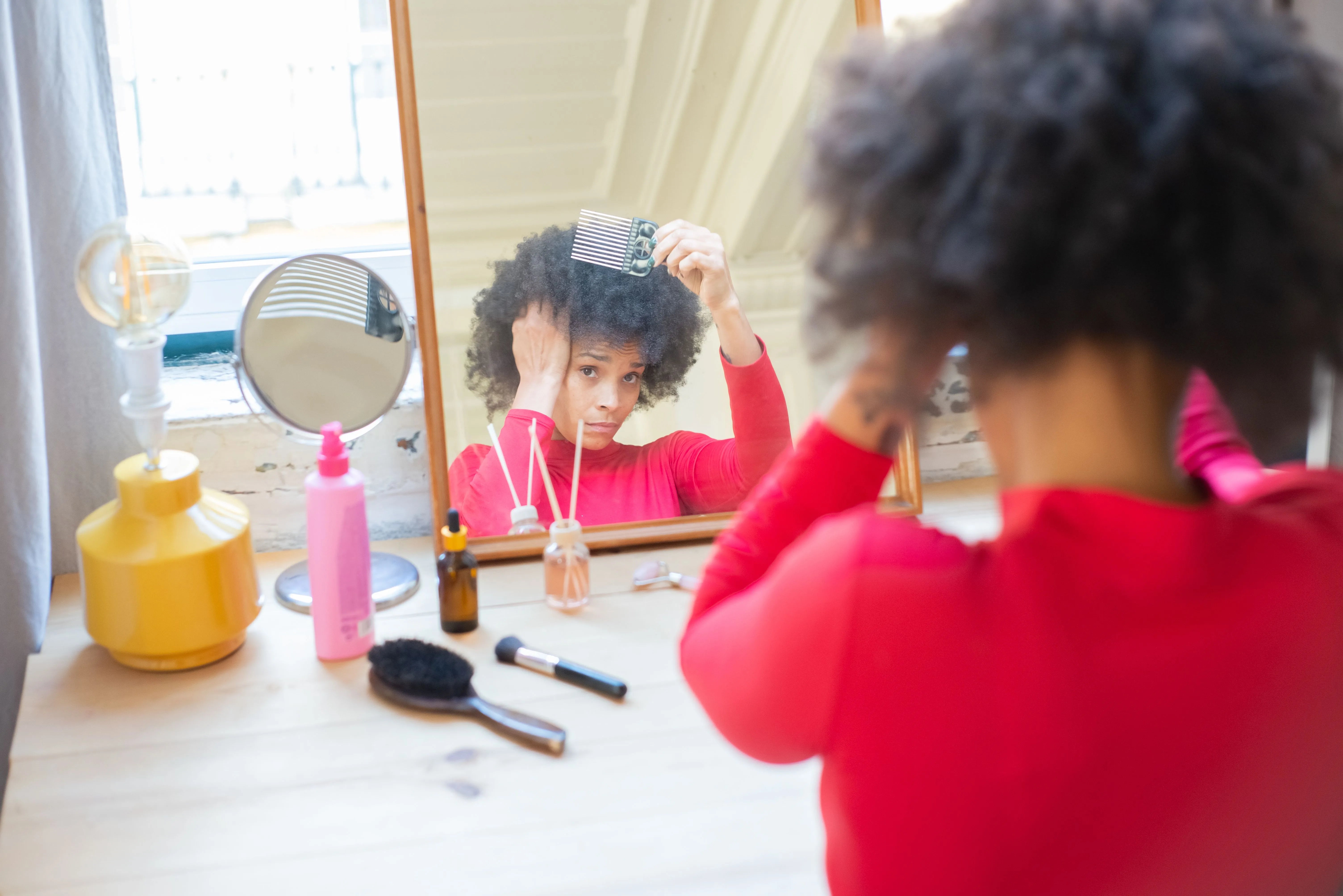 Woman combing her hair while looking in a bathroom mirror as part of her hair care routine