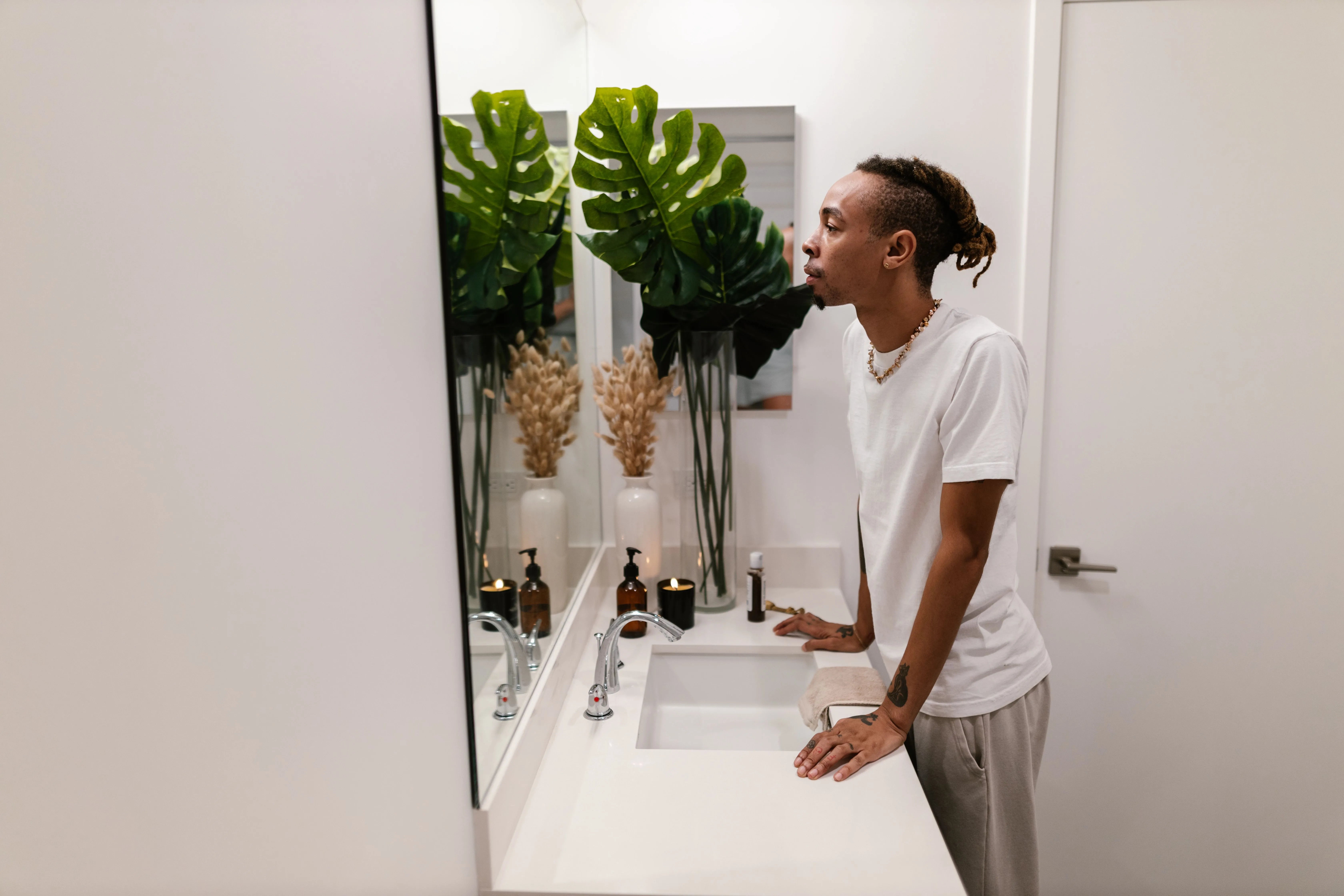 Man standing at a bathroom sink examining his reflection in the mirror while considering his hair loss treatment options