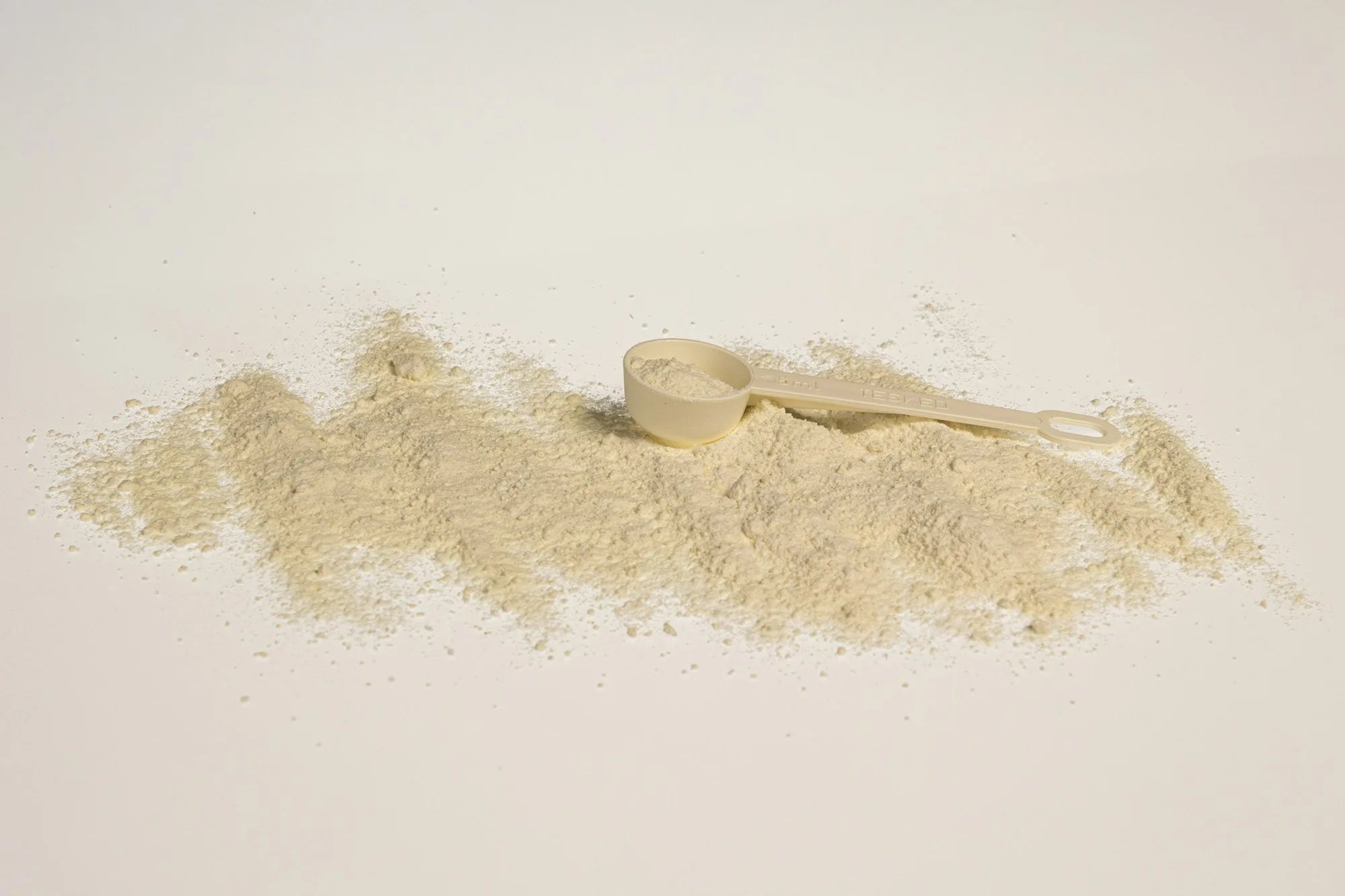 A measuring scoop resting in a pile of fine collagen powder on a white background, illustrating the hydrolyzed collagen supplement used to support hair follicle structure
