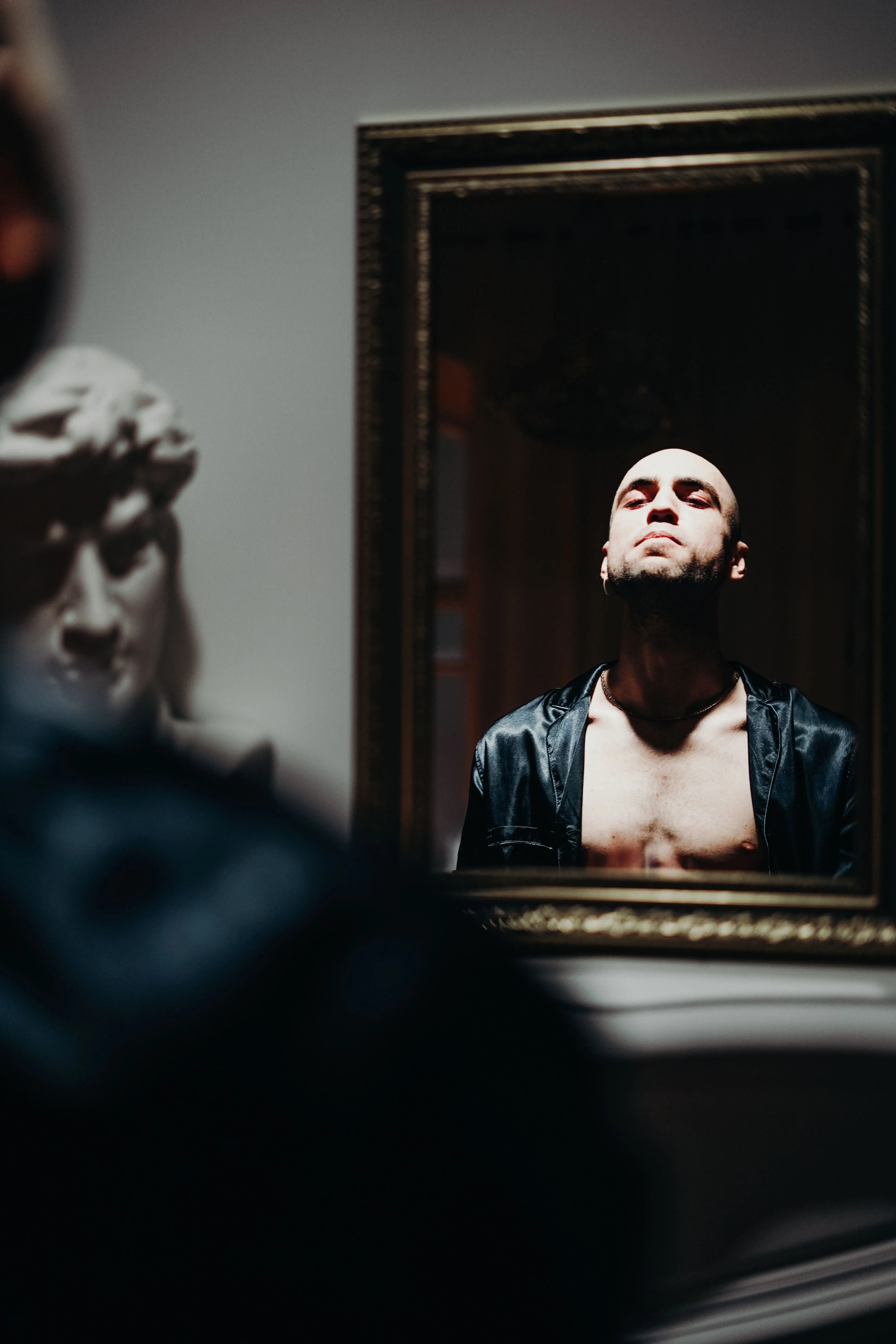 Man examining his reflection in a dimly lit mirror, contemplating hair loss and treatment options