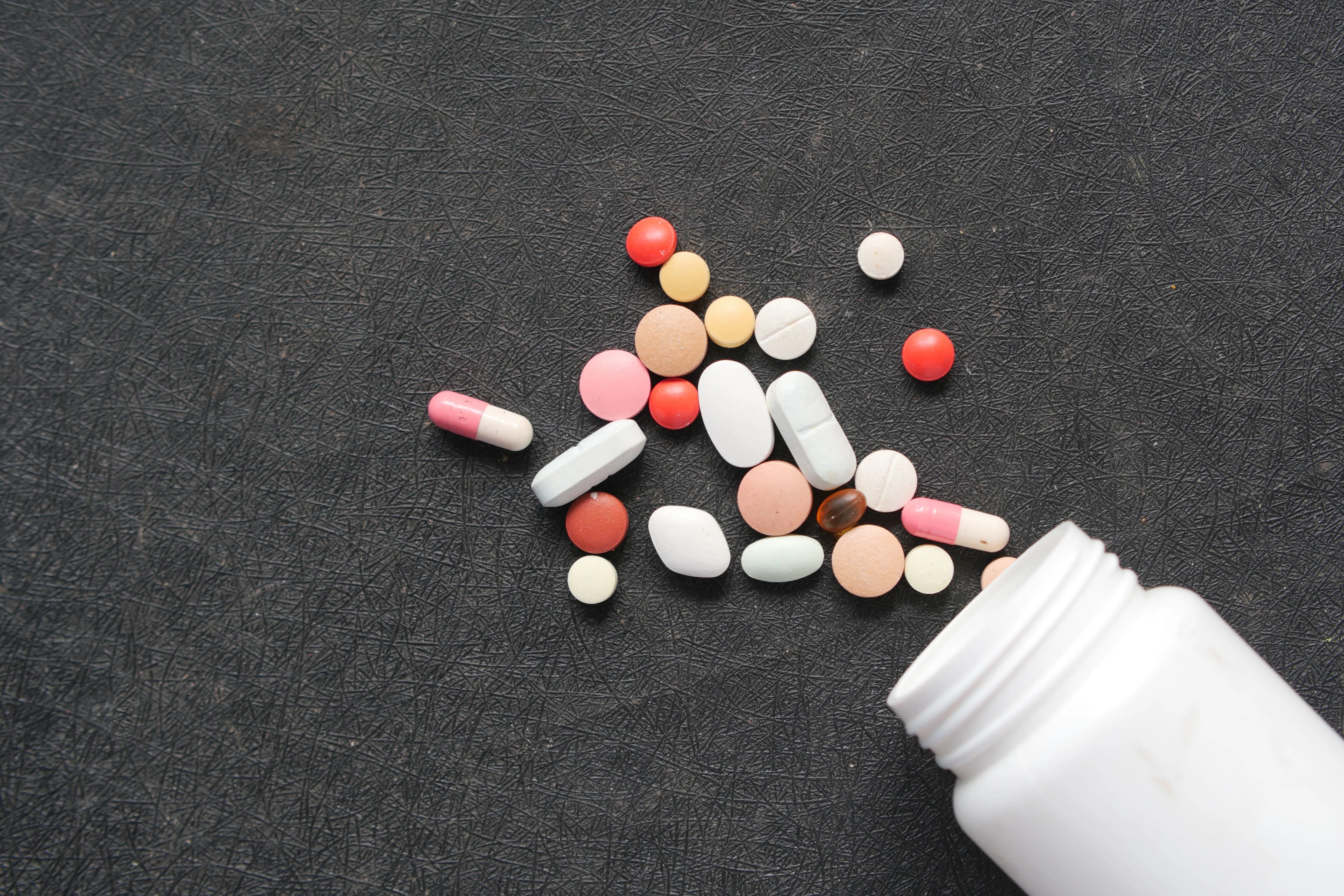 Assorted medication pills and capsules spilled from a bottle onto a dark surface, representing oral drug treatments like JAK inhibitors