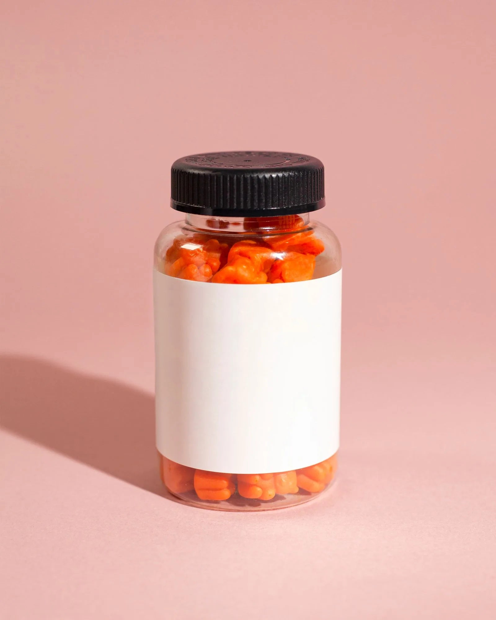 Clear bottle of orange hair vitamin gummies on a soft pink background, unbranded product shot for a gummy supplement comparison