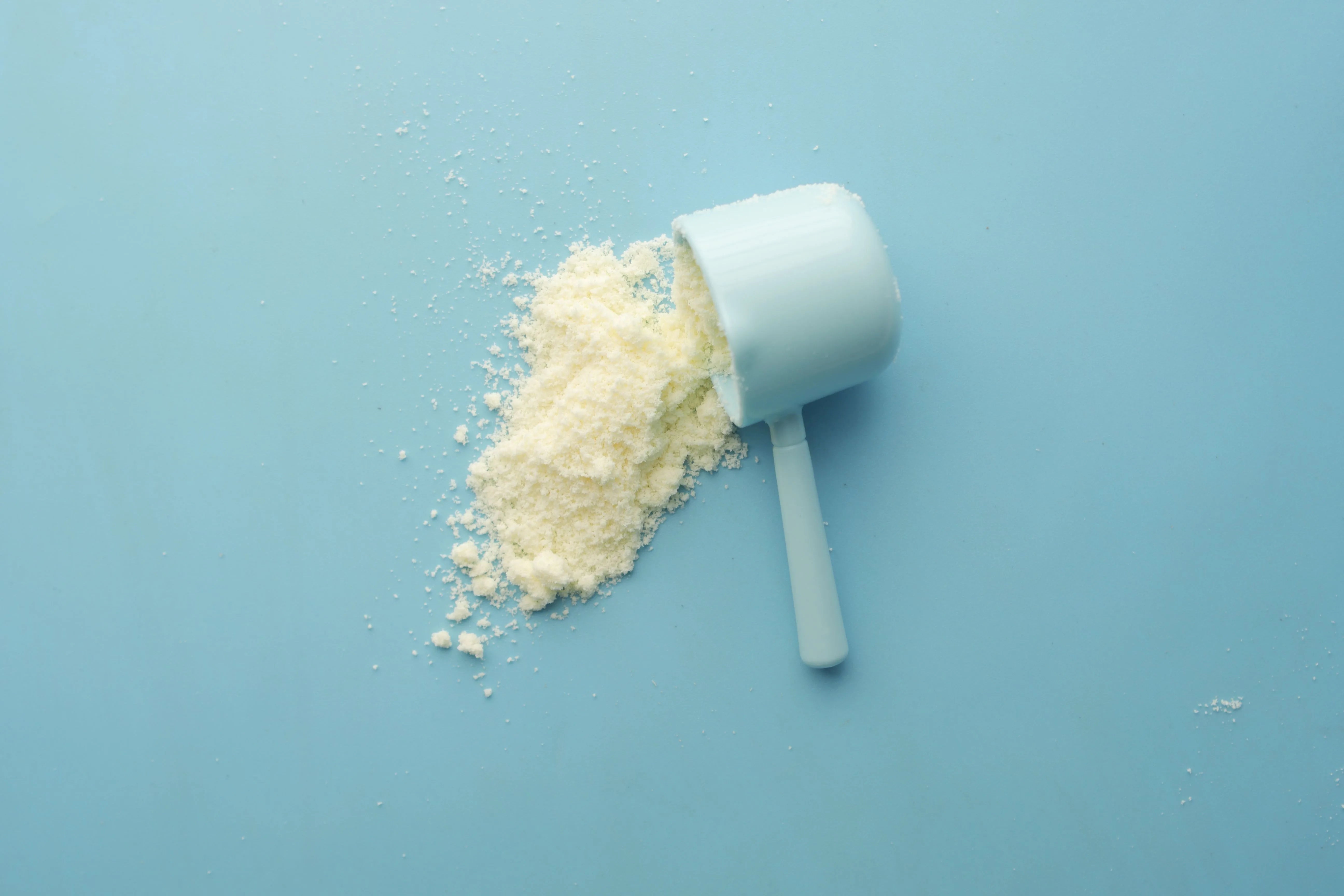 Fine white MSM supplement powder spilling from a measuring scoop, showing the pure sulfur compound used in hair growth supplementation