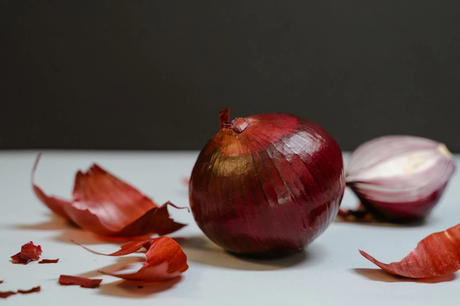 Fresh whole and sliced red onions with papery skins on a light surface, the raw ingredient behind the onion juice hair growth trend