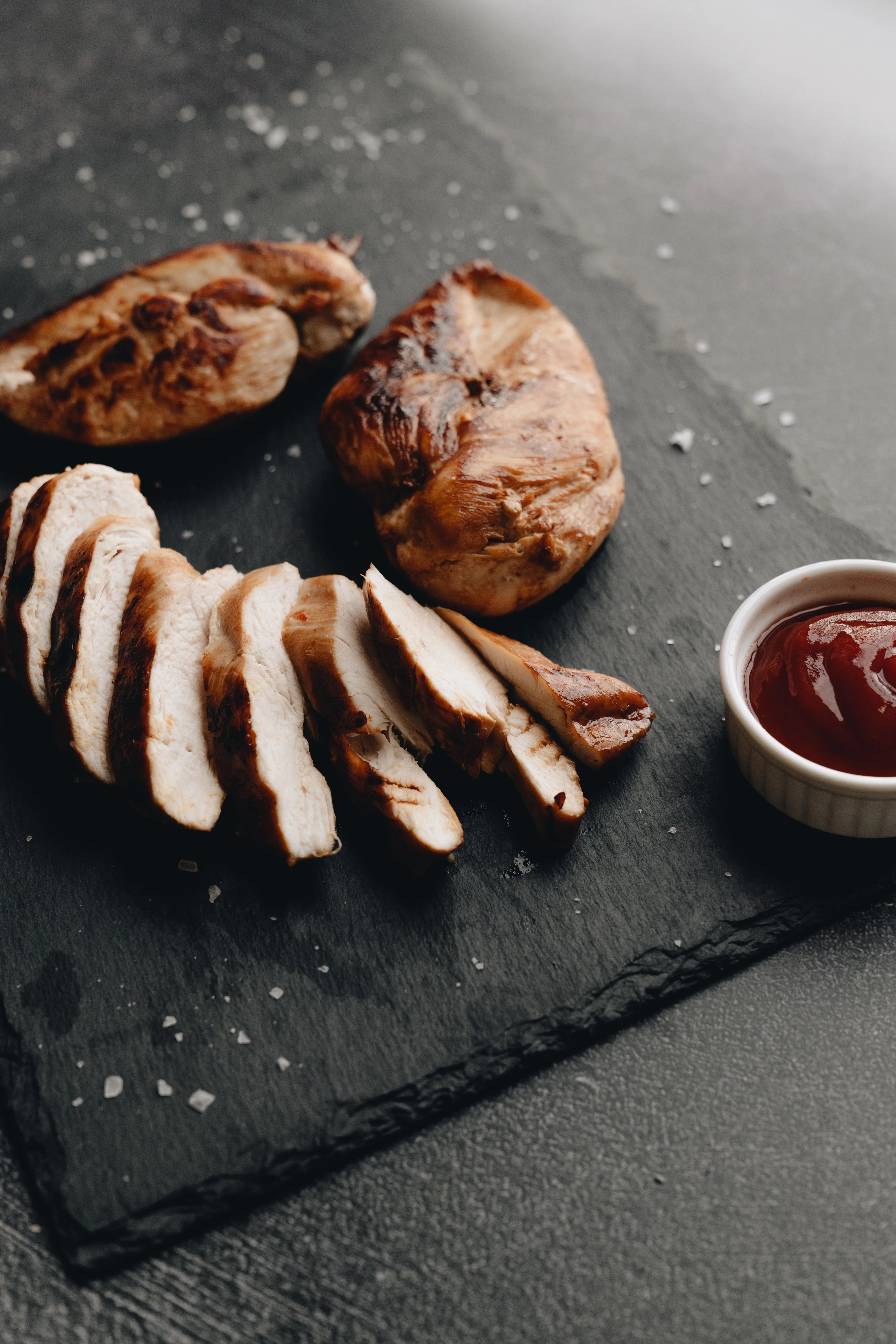 Sliced grilled chicken breast, a lean protein source important for healthy hair growth, served on a dark slate plate