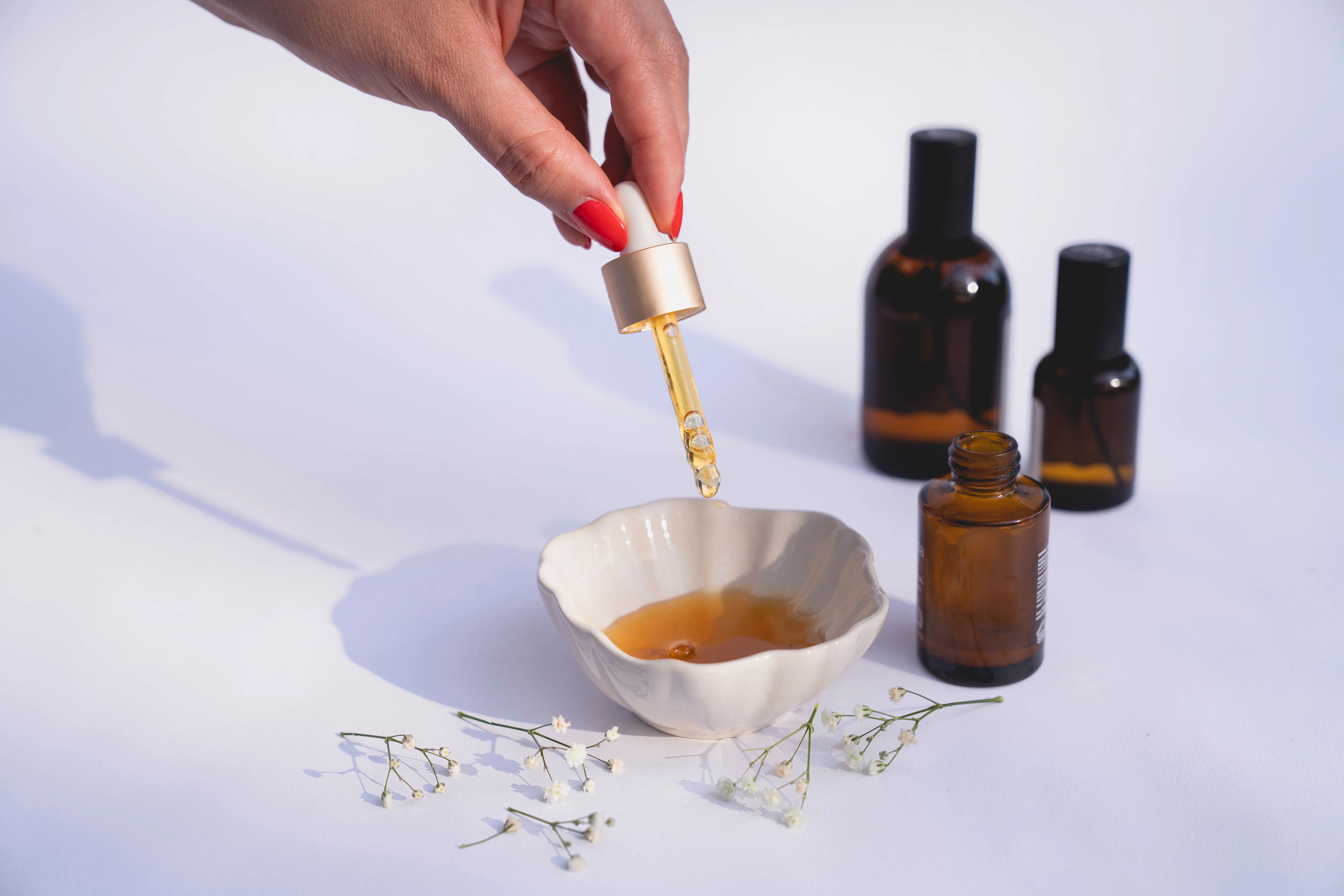 Close-up of a hand using a glass dropper to apply hair serum into a small bowl, with amber glass bottles in the background, representing a complete hair care routine system
