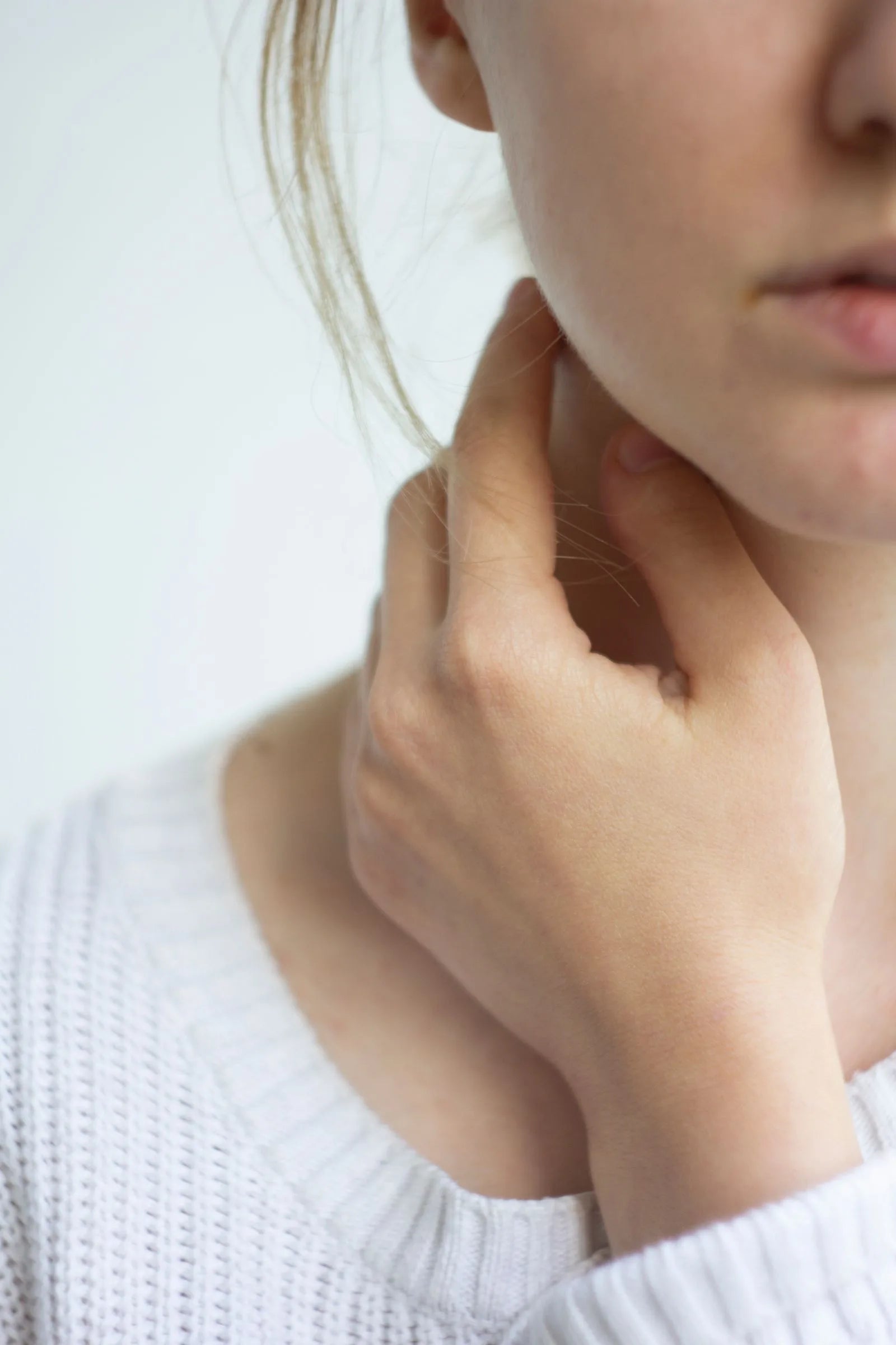 Close-up of a woman gently touching her neck and throat, the area where the thyroid gland is located