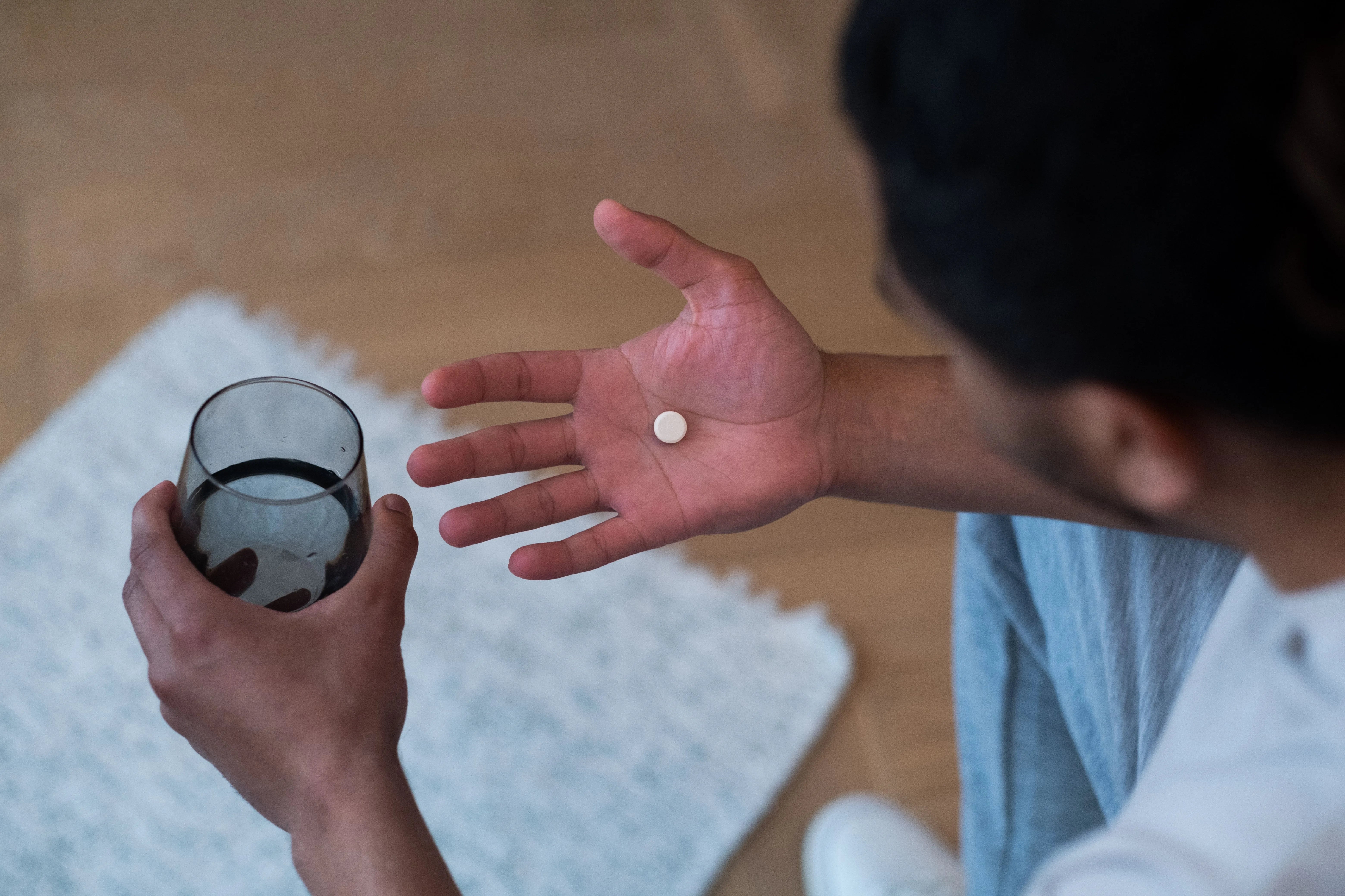 Close up of a hand holding a single pill next to a glass of water, representing an oral hair loss treatment