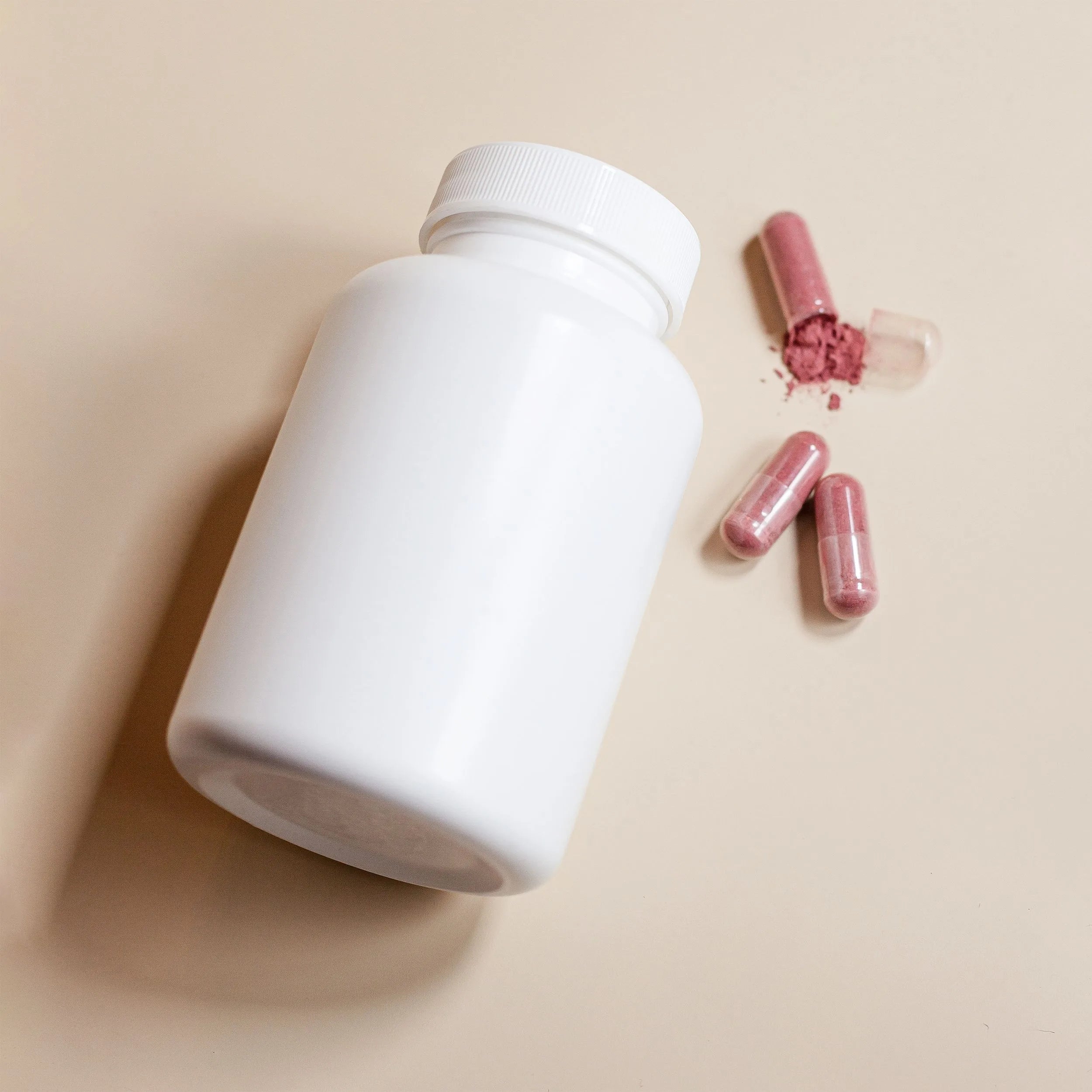 An unlabeled white supplement bottle lying next to loose capsules on a neutral tan background, representing a generic hair growth supplement product