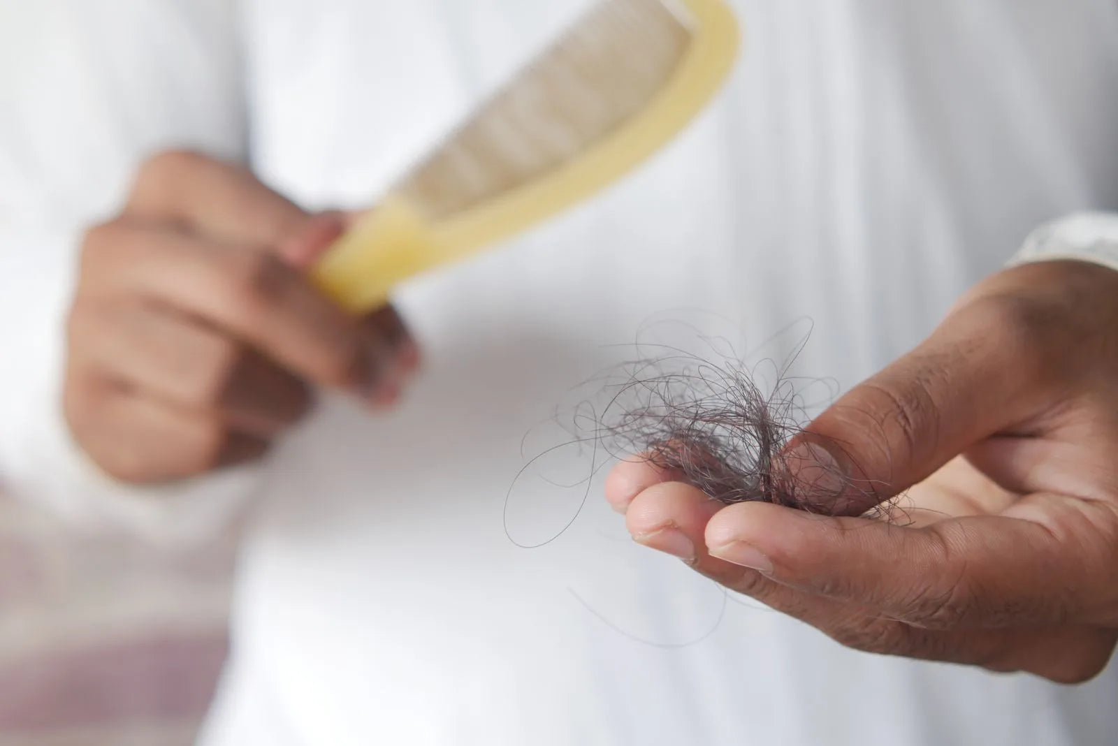 Close-up of a hand holding a comb with several loose strands of hair caught in the teeth, illustrating increased hair shedding